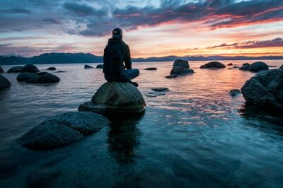 man thinking on rock surrounded by water